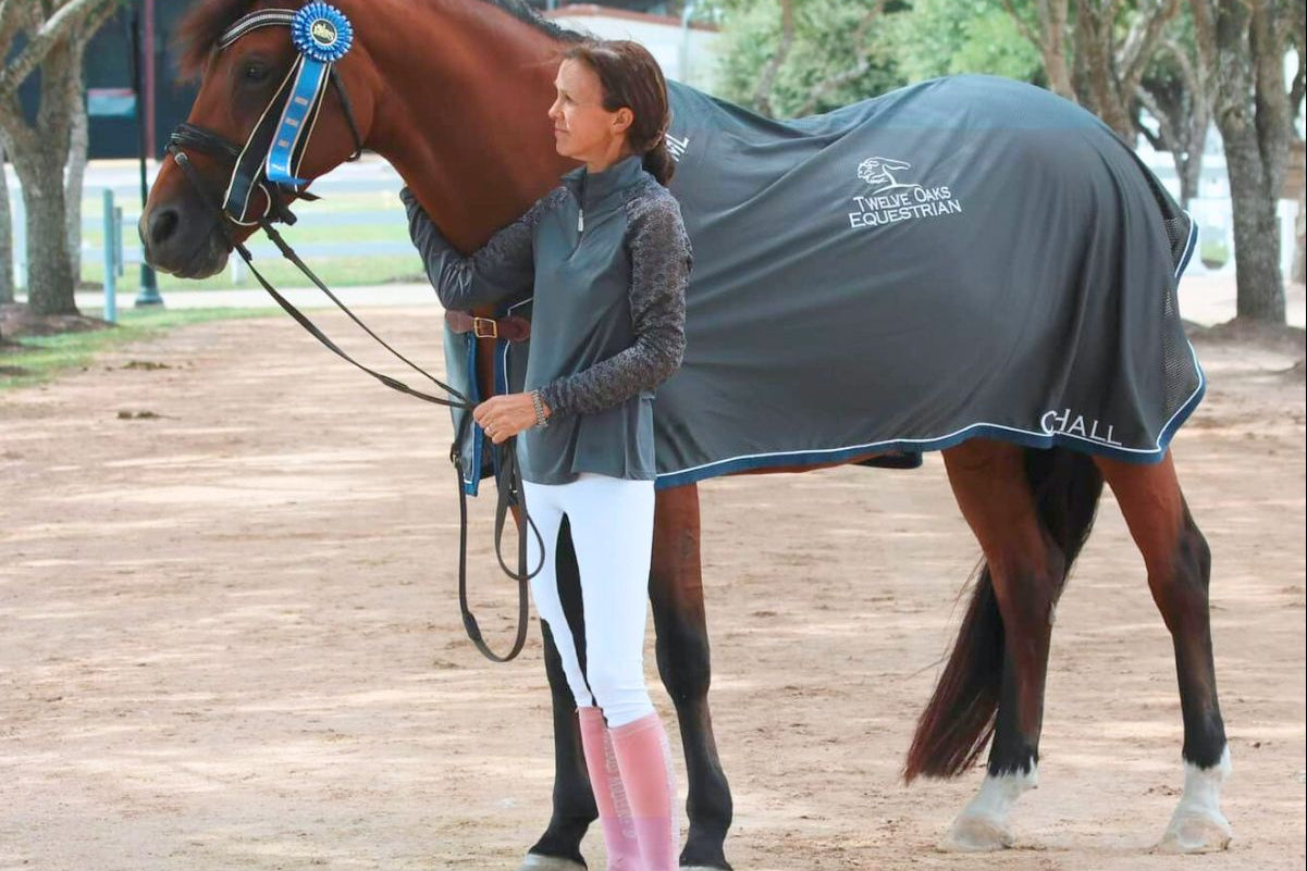 Woman standing next to a horse wearing a  Stitch Horse (TSH) custom gray scrim sheet, with logo, name and additional text embroidery. 